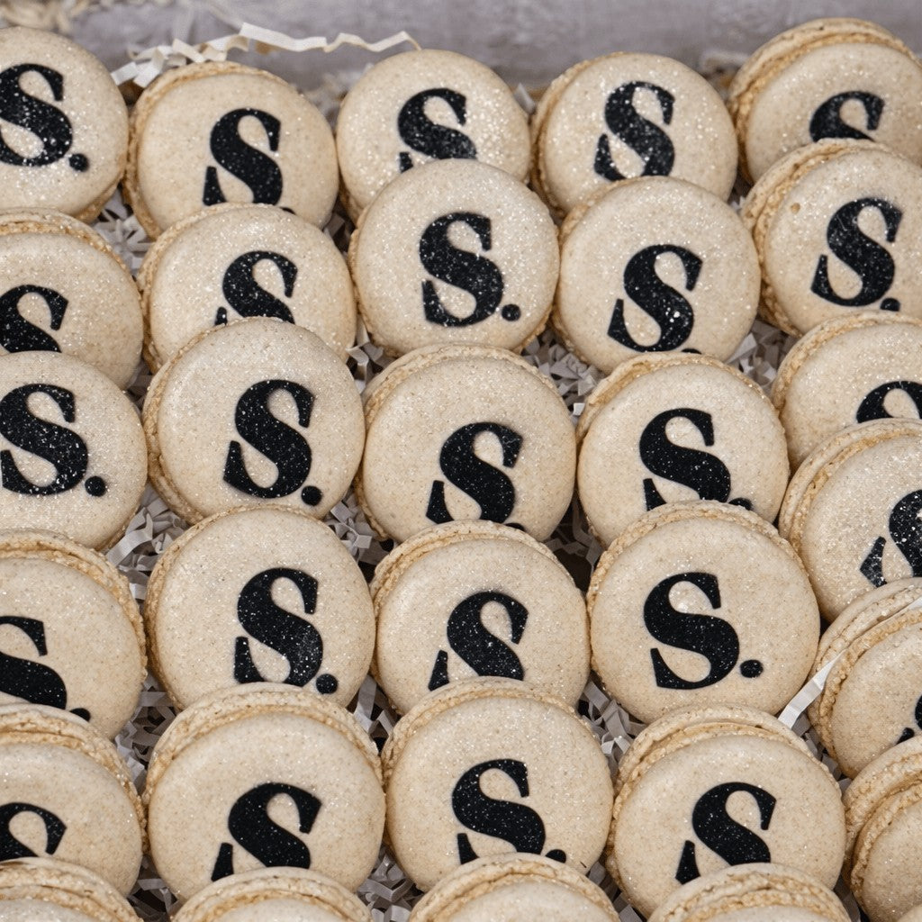 Sweet Snap Sydney beige macarons with black 'S' logo and glitter, perfect for corporate events.