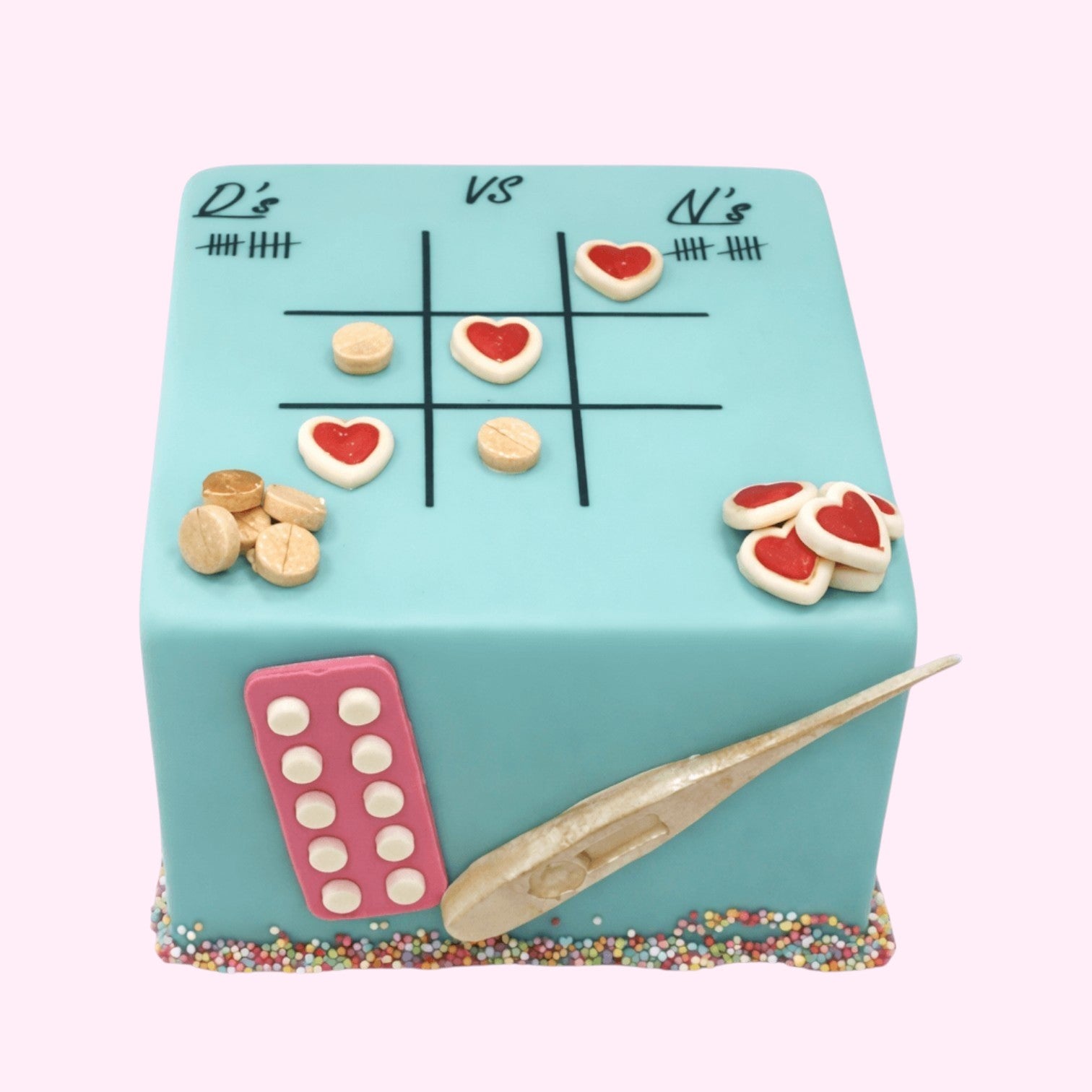 Sweet Snap Sydney square cake with a tic-tac-toe game, hearts, pills, and a thermometer decoration. Blue icing with colourful sprinkles.